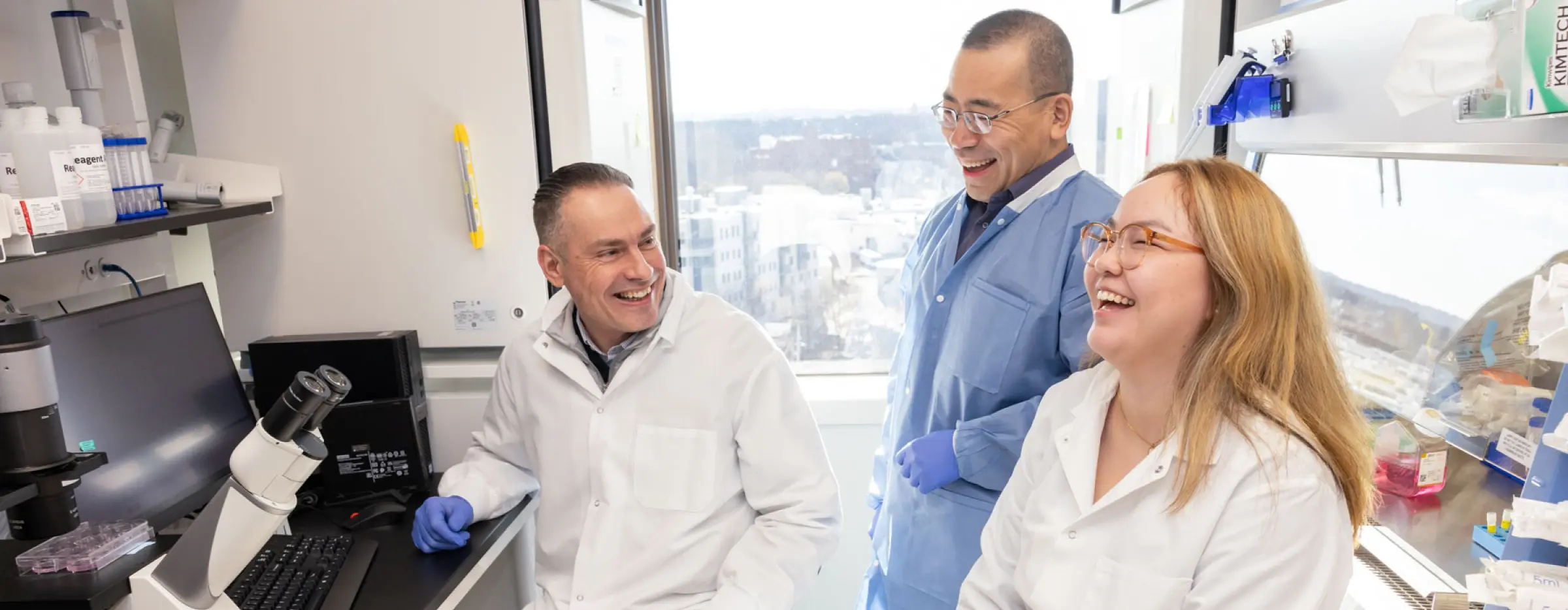 Three colleagues laughing in lab attire.